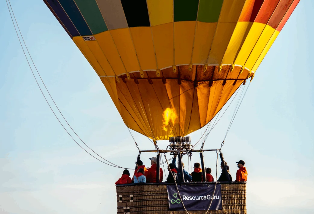 Resource Guru staff on a hot air balloon ride with a Resource Guru banner strung over the side of the basket.