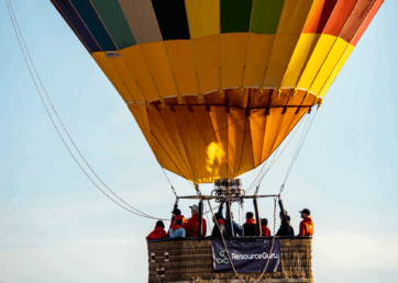 Resource Guru staff on a hot air balloon ride with a Resource Guru banner strung over the side of the basket.